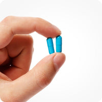 For Conceive Plus Couples Bundle Fertility Support | His/Her Deal (FR), image of the close-up of a hand holding two bright blue capsules from men's fertility support supplement, showing capsule size and texture, ideal for illustrating dosage form on a white background.