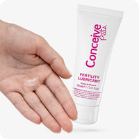 Conceive Plus Fertility Lubricant Tube (FR) placed beside an open left hand showing a clear portion of lubricant gel on the palm. The 75ml tube, labeled in pink and white, emphasizes its French origin and fertility-enhancing ingredients.