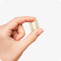 Conceive Plus Ovulation Support (FR) capsules held between fingers, showing two translucent beige capsules close-up to highlight their compact, easy-to-swallow size and smooth texture, ideal for daily ovulation support.