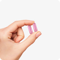 Conceive Plus Women's Fertility Support (FR) capsules held between fingers, showcasing two pink capsules against a white background—highlighting size, smooth texture, and daily dosage clarity of fertility supplement for women.