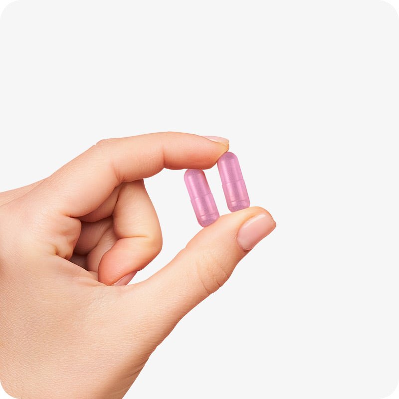 Conceive Plus Women's Fertility Support (FR) capsules held between fingers, showcasing two pink capsules against a white background—highlighting size, smooth texture, and daily dosage clarity of fertility supplement for women.